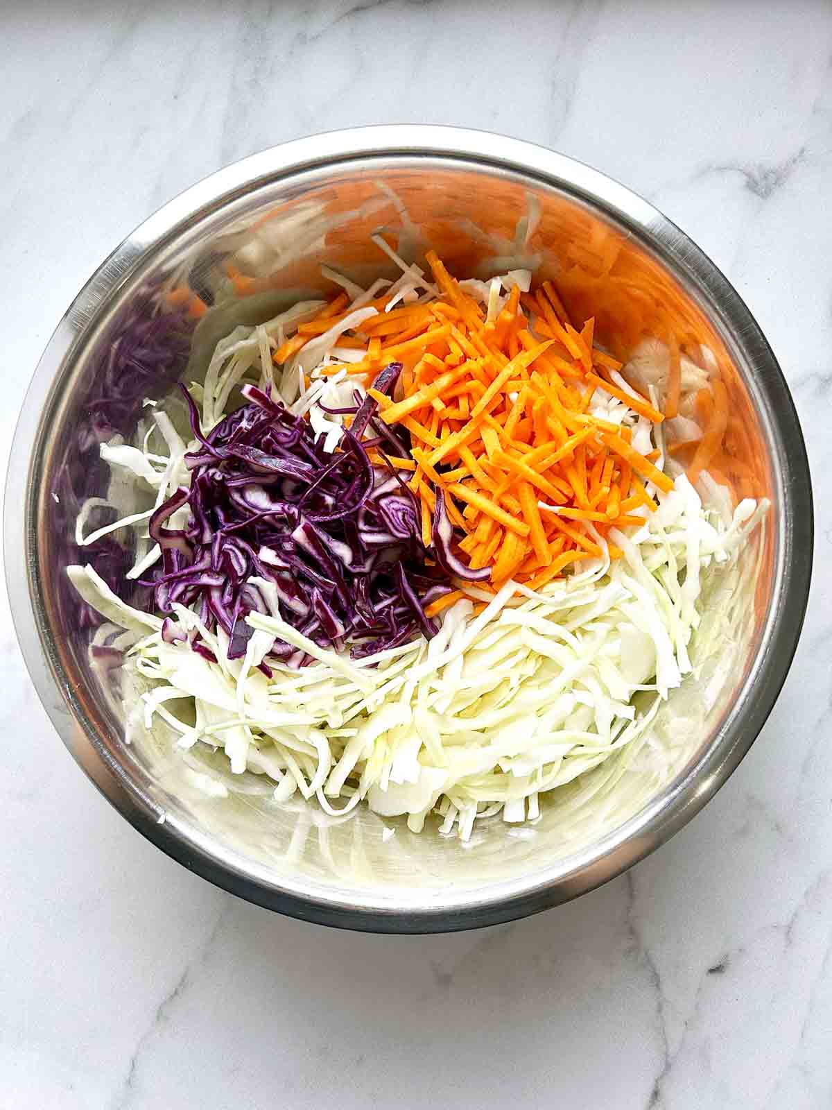 green cabbage, purple cabbage, and carrots arranged in bowl.