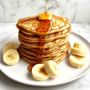 stack of banana pancakes on plate with maple syrup drizzled on top.