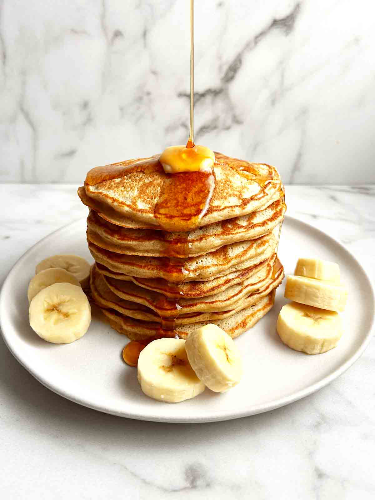 stack of banana pancakes on plate with maple syrup drizzled on top.