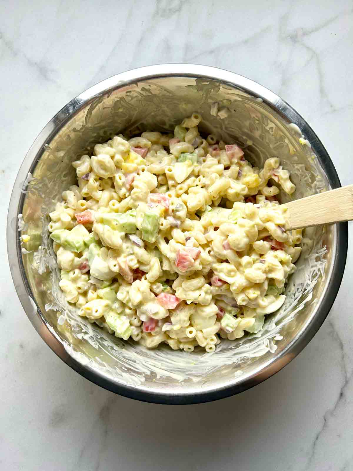 macaroni salad being mixed together in bowl.