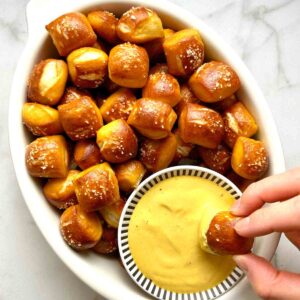 pretzel bite being dipped into honey mustard sauce.