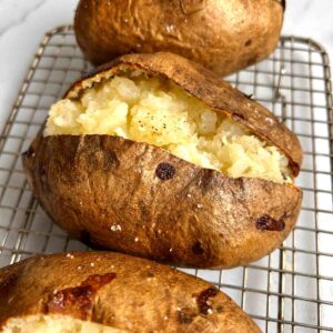 3 baked potatoes on wire rack; split open to show inside of potatoes.