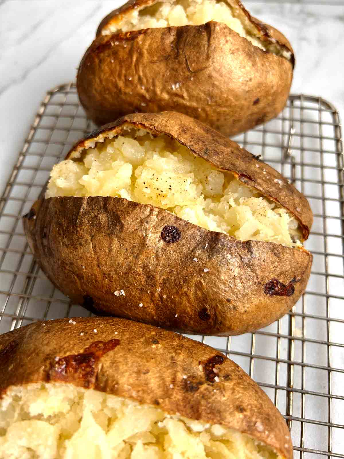 3 baked potatoes on wire rack; split open to show inside of potatoes.