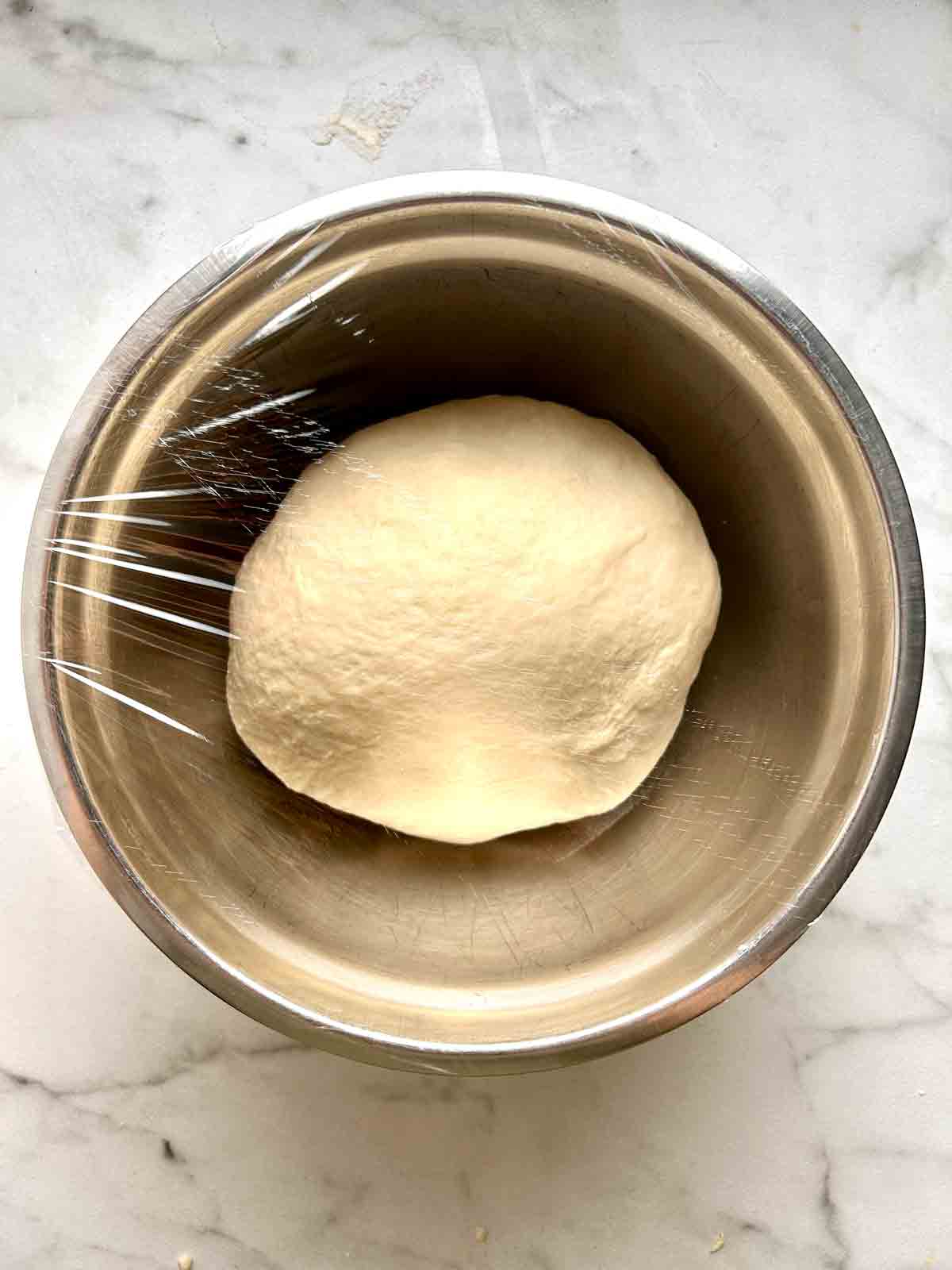 kneaded dough resting in bowl with plastic wrap over top.
