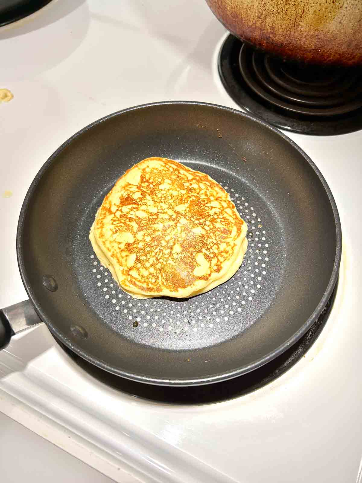 pancake flipped in pan; golden brown exterior on one side.