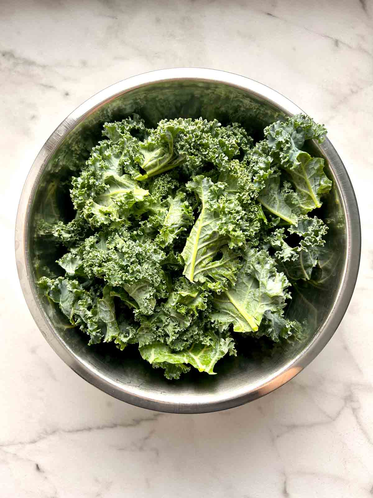 kale pieces tossed with olive oil in bowl.