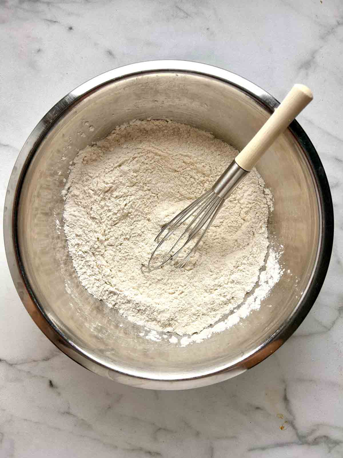 flour and other dry ingredients being whisked in bowl.