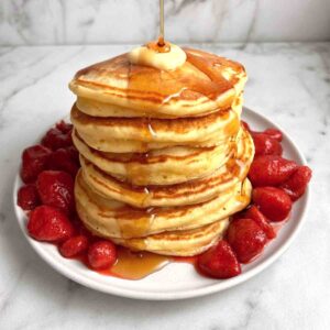 stack of sour cream pancakes with maple syrup and strawberries.