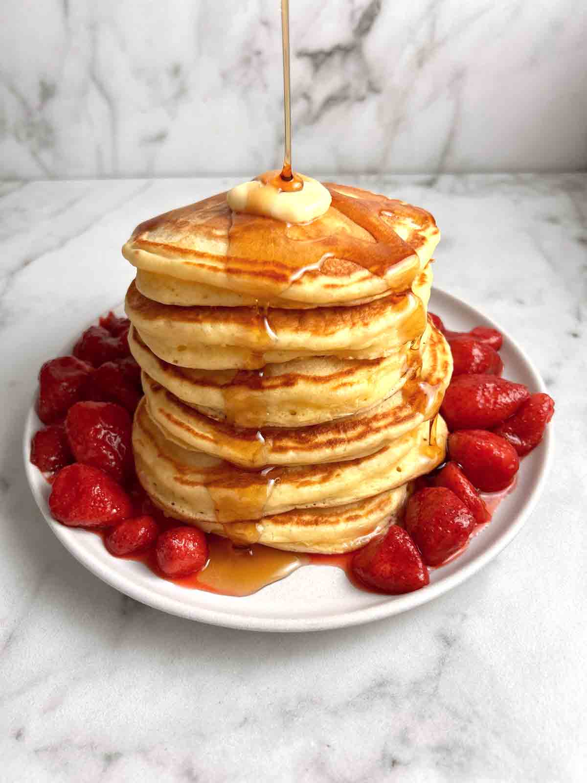 stack of sour cream pancakes with maple syrup and strawberries.