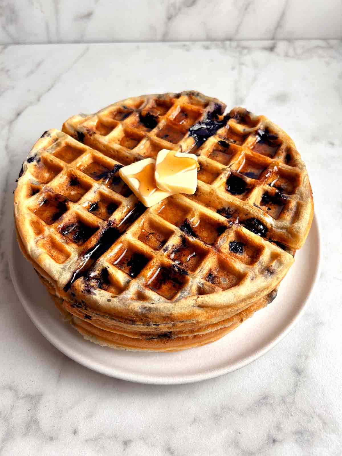 plate of blueberry waffles with syrup and butter on top.
