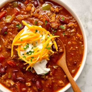 close up of chili with sour cream and cheddar cheese on top.