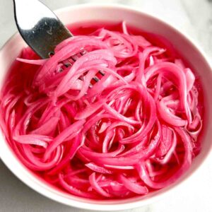 fork lifting pickled red onions from bowl.