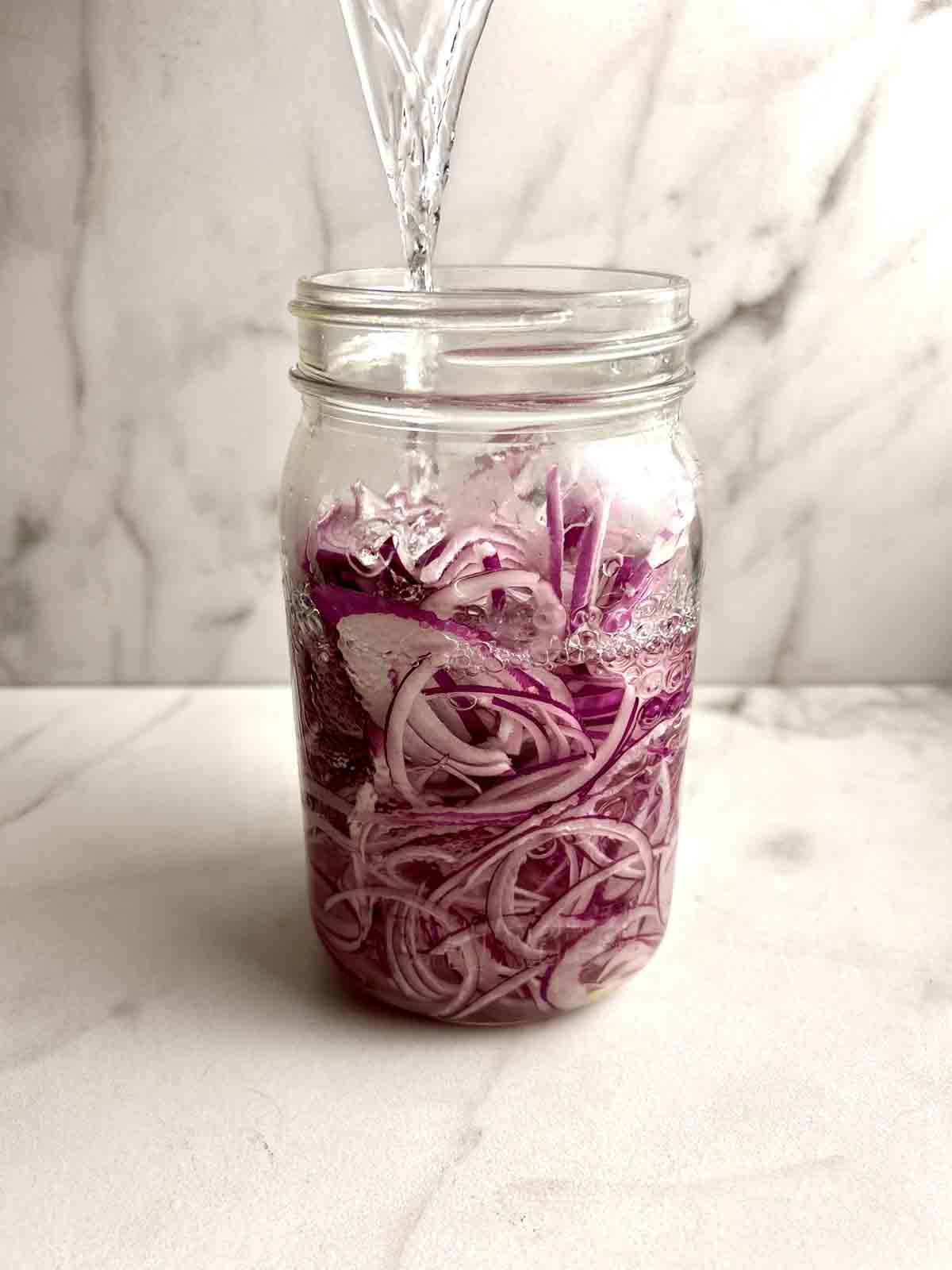 brine being poured over onions in jar.