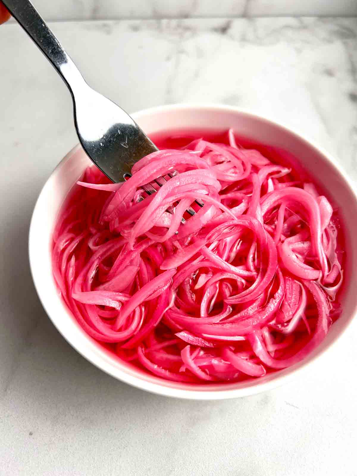 fork lifting pickled red onions from bowl.