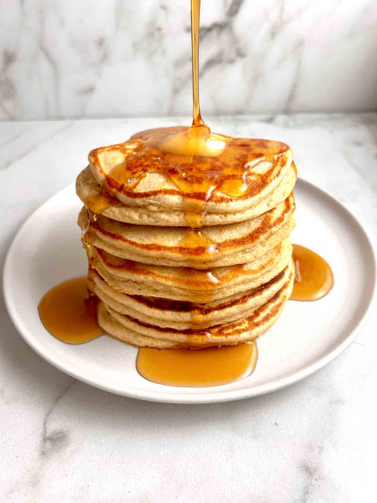 stack of protein pancakes with maple syrup drizzling over top of them.