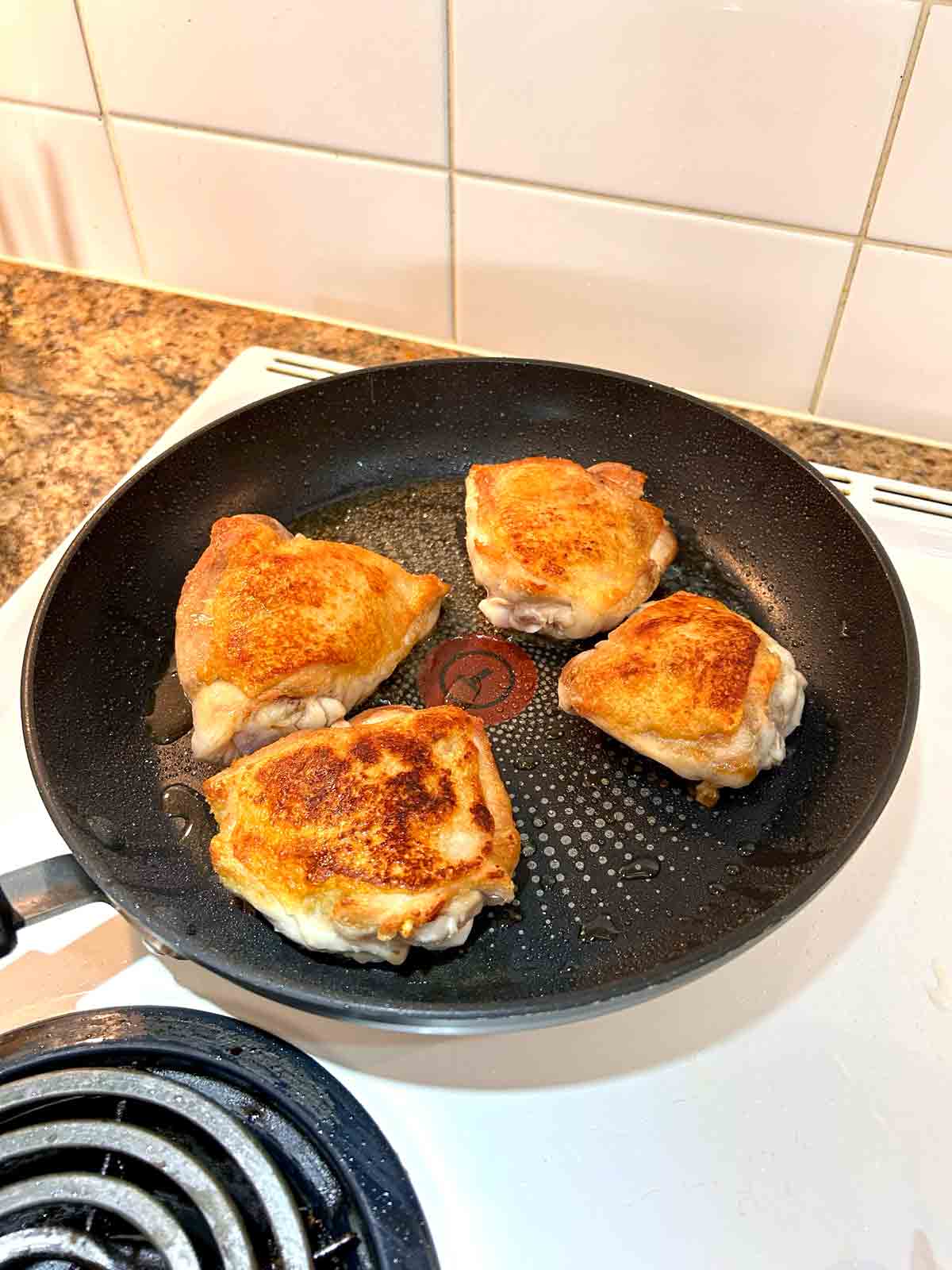 meat side of chicken thighs frying in pan.