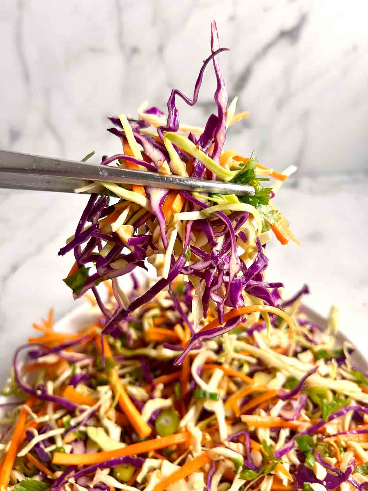 chopsticks lifting Asian coleslaw from bowl.