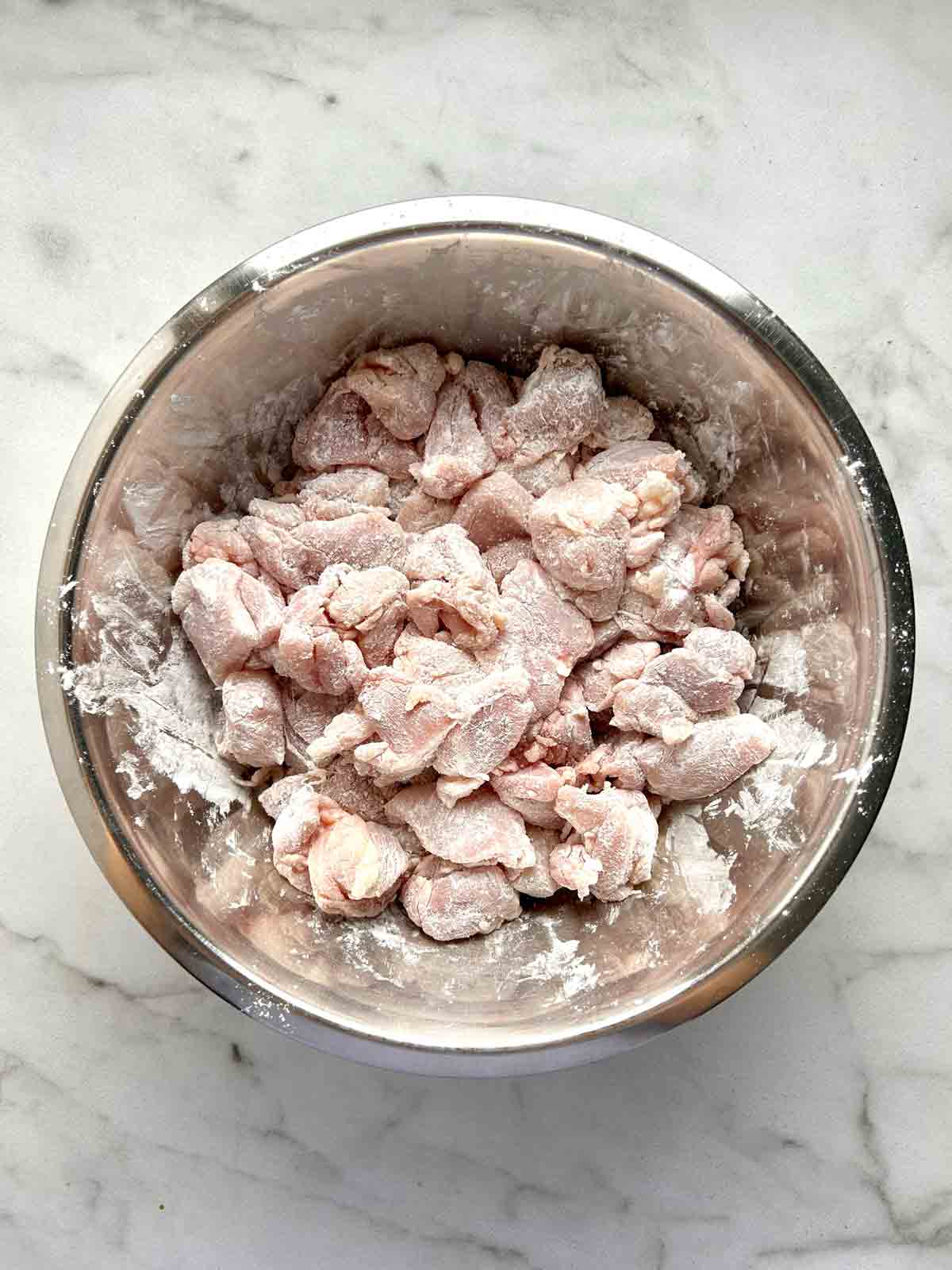 chicken pieces being coated in cornstarch.