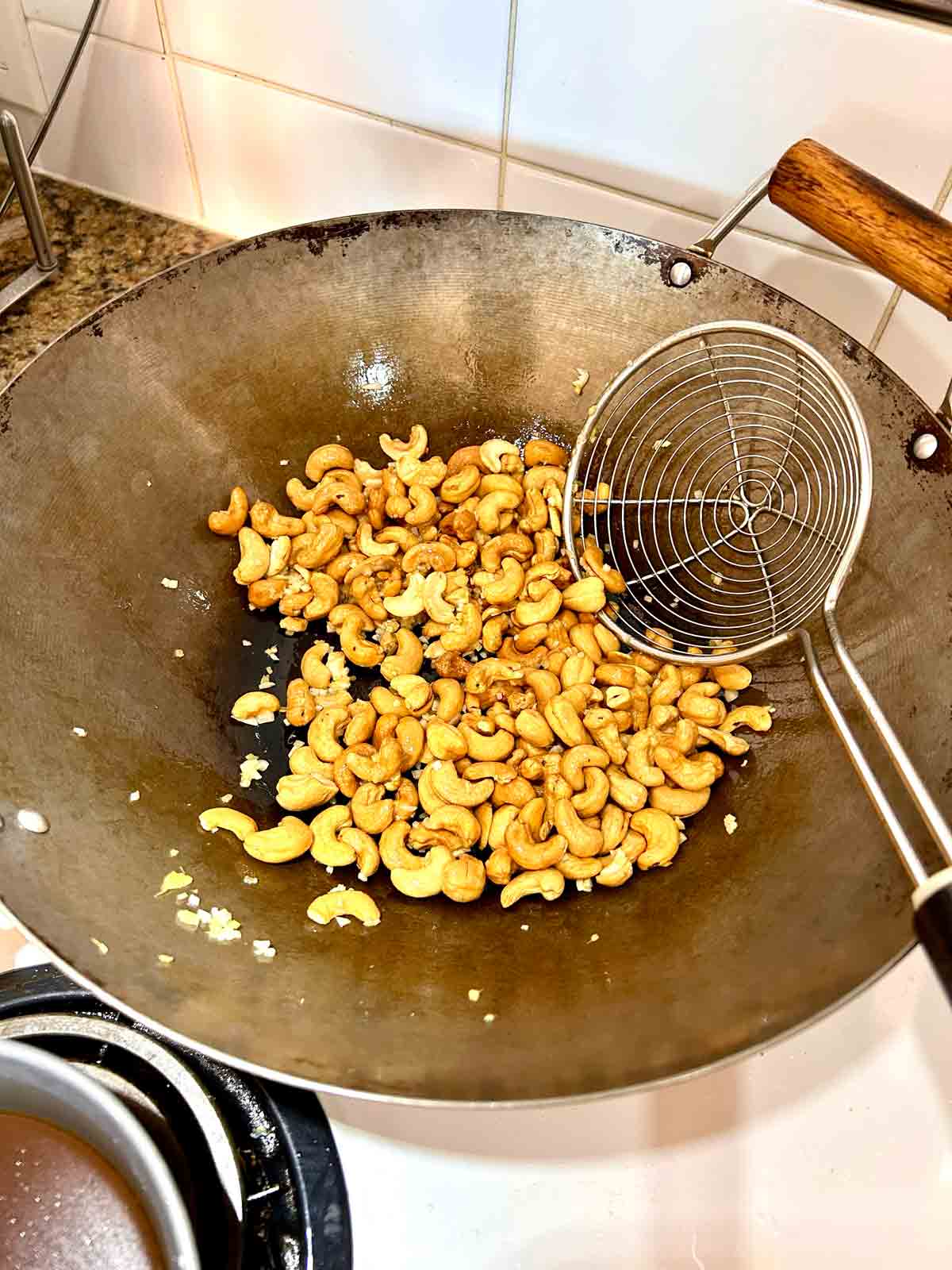 garlic, ginger, and cashews being sautéed in wok.