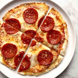 close up of tortilla pizza cut into slices on plate.