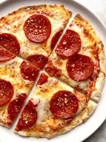 close up of tortilla pizza cut into slices on plate.