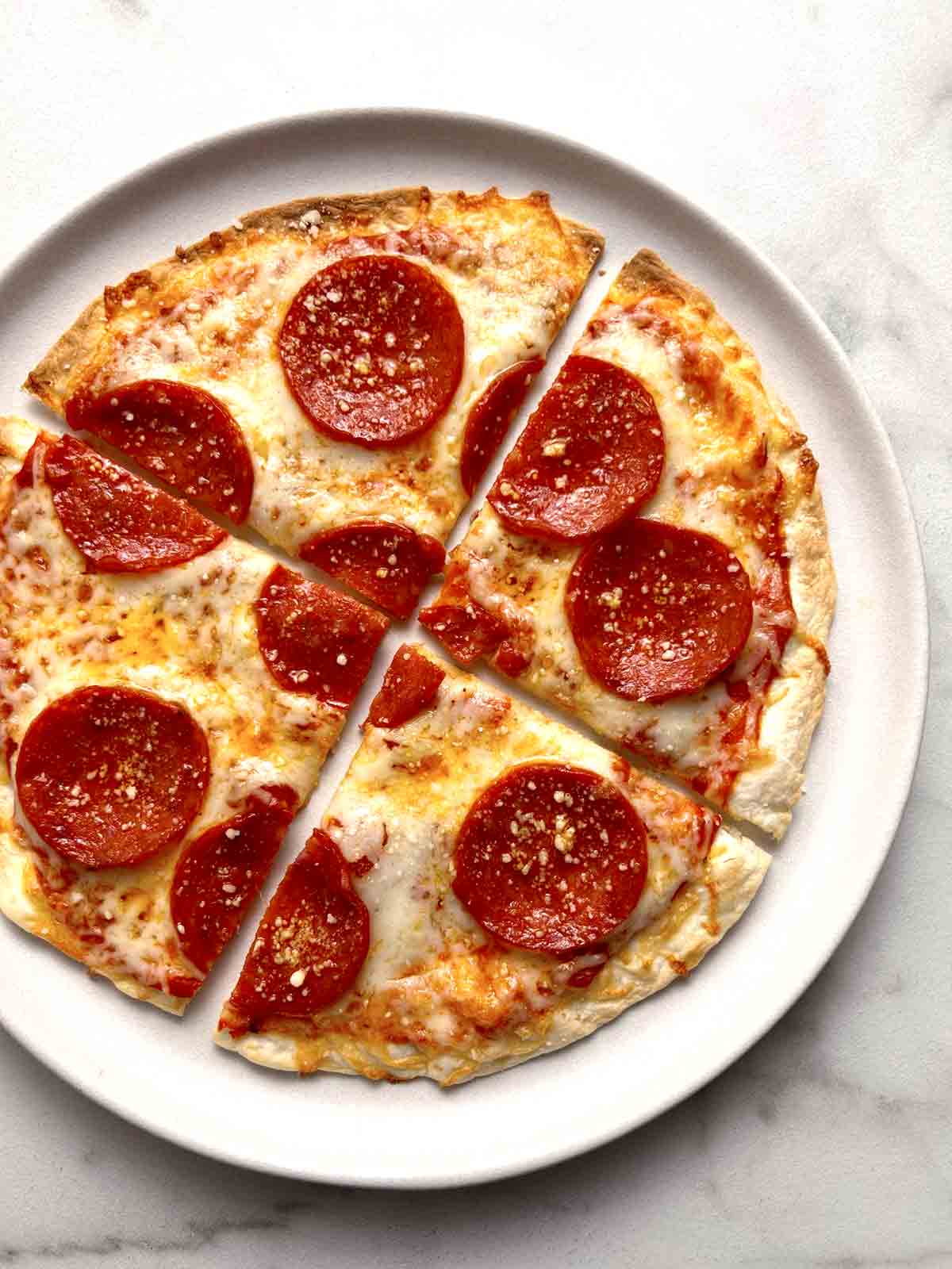 close up of tortilla pizza cut into slices on plate.