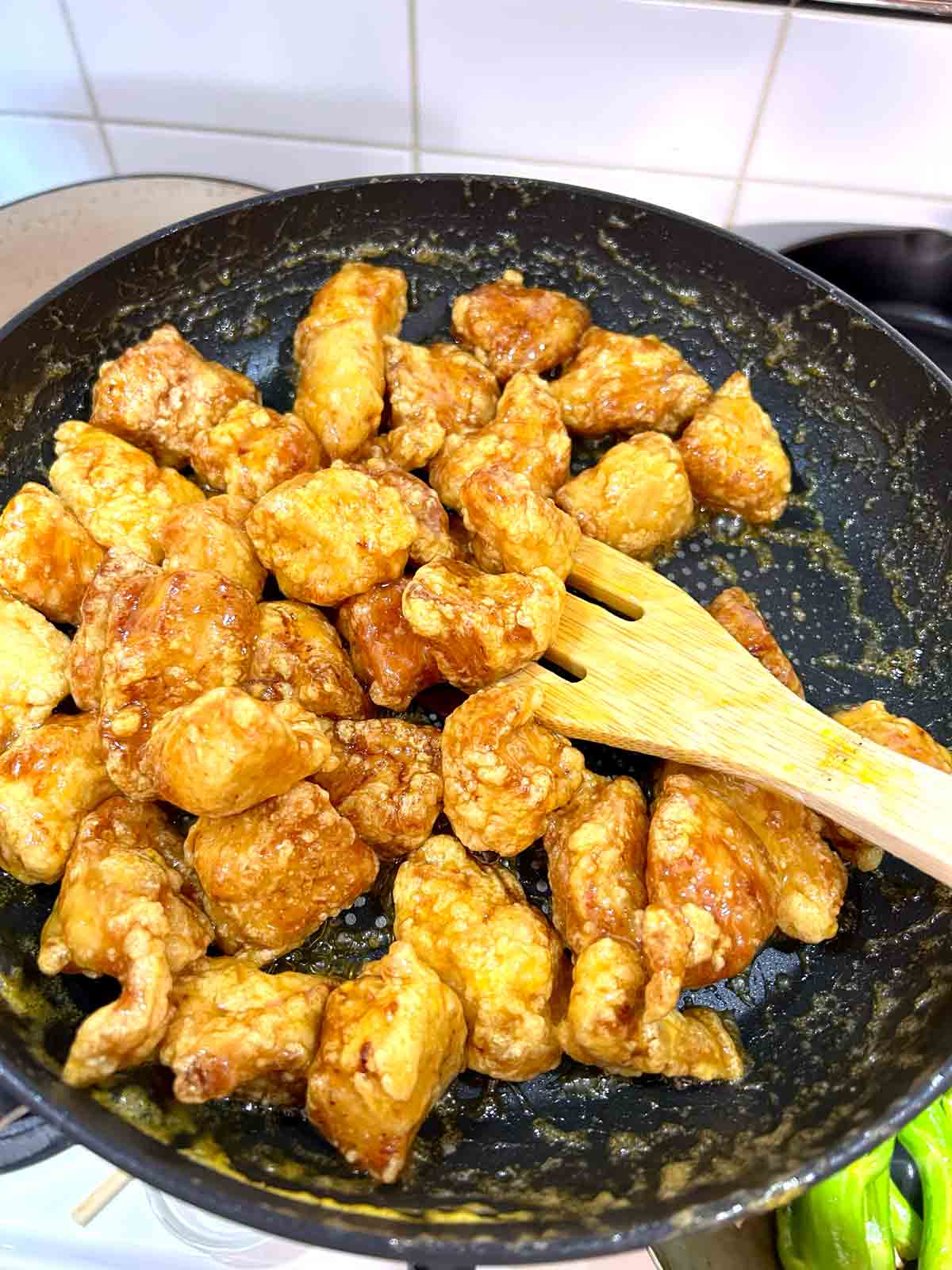 fried chicken being tossed with orange sauce in pan.
