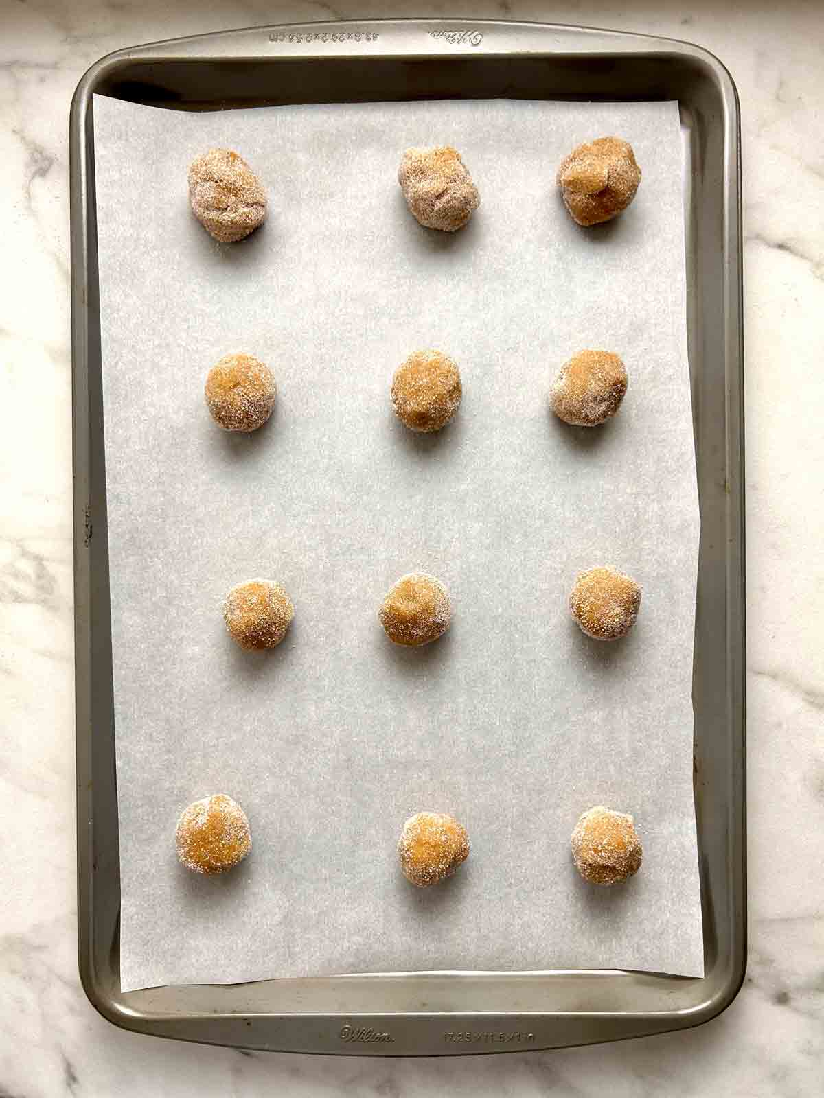 dough shaped into balls, rolled in sugar, and placed on baking sheet.