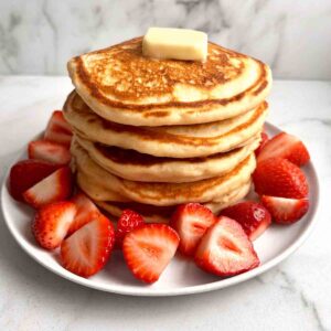 stack of pancakes with freshly chopped strawberries around it.