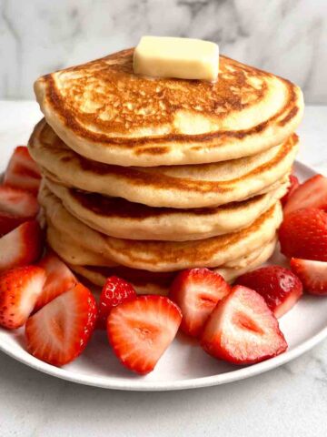 stack of pancakes with freshly chopped strawberries around it.