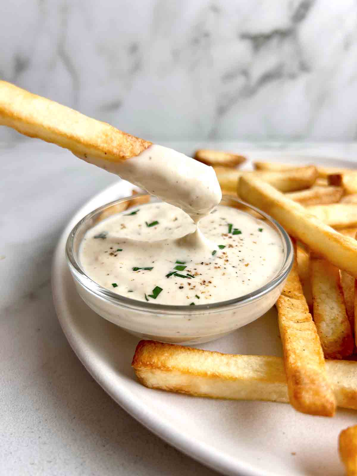 fry being dipped into bowl of aioli.