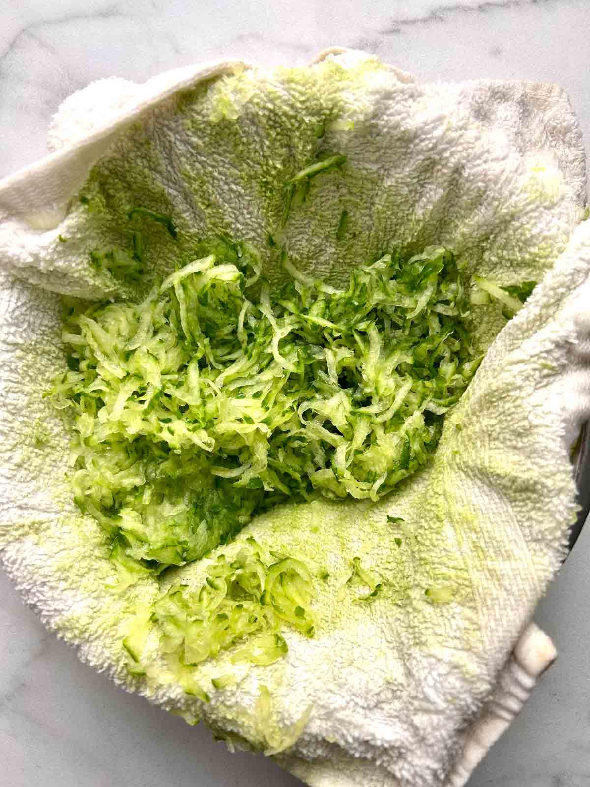 grated cucumber being squeezed in kitchen towel.