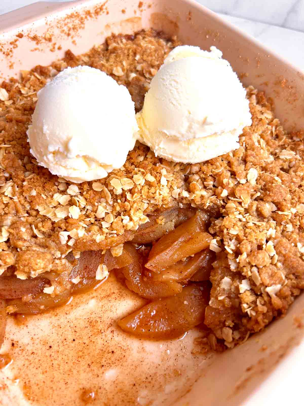 apple crisp in baking dish with two scoops of ice cream on top.