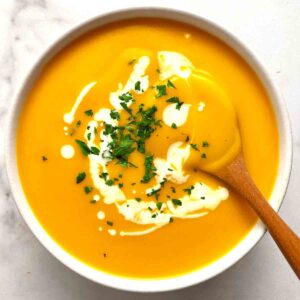 bowl of butternut squash soup with parsley and cream on top.