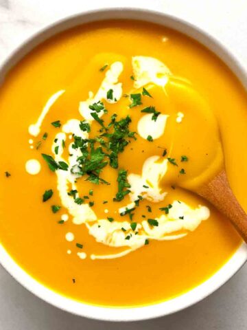 bowl of butternut squash soup with parsley and cream on top.