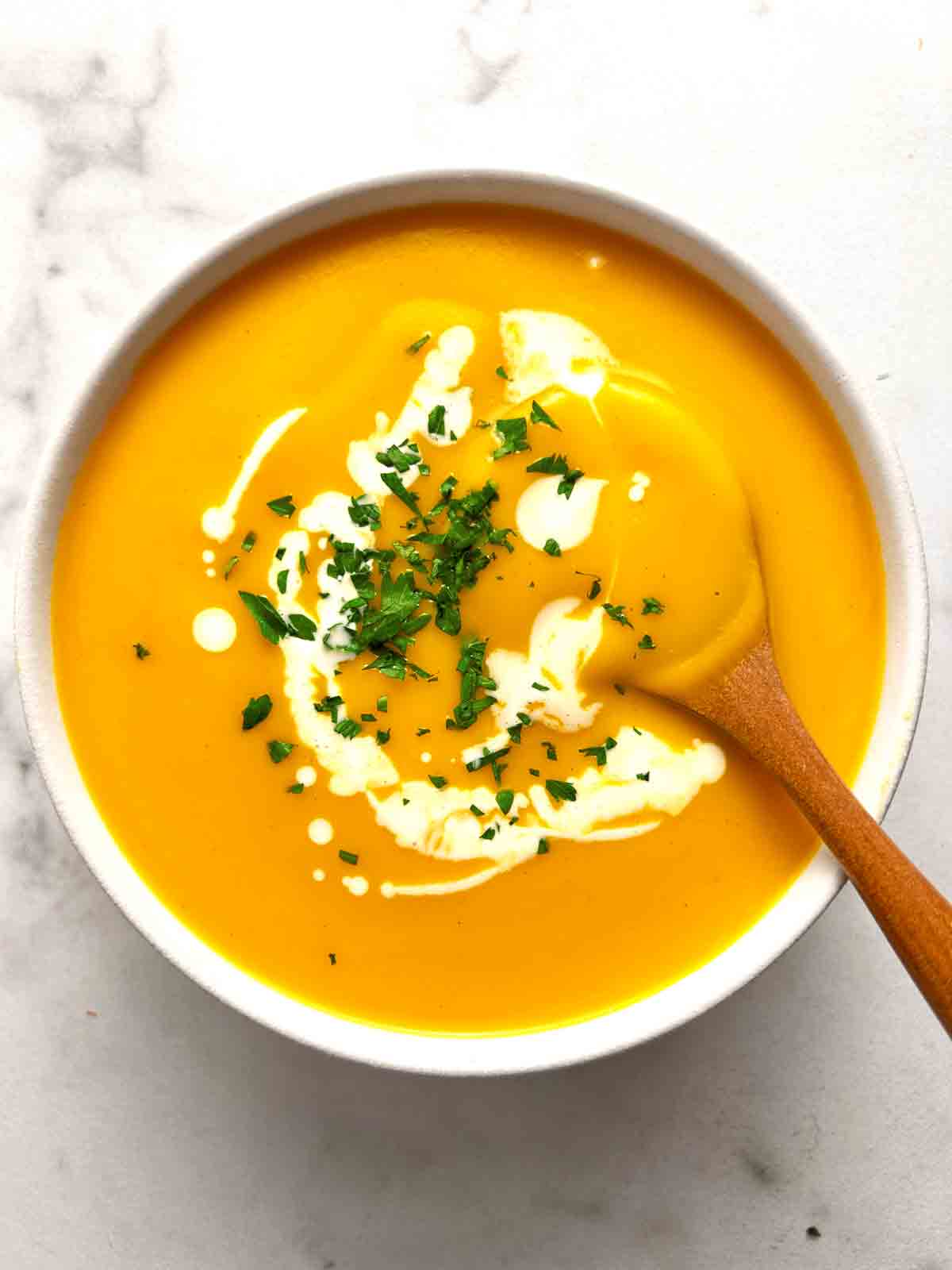 bowl of butternut squash soup with parsley and cream on top.