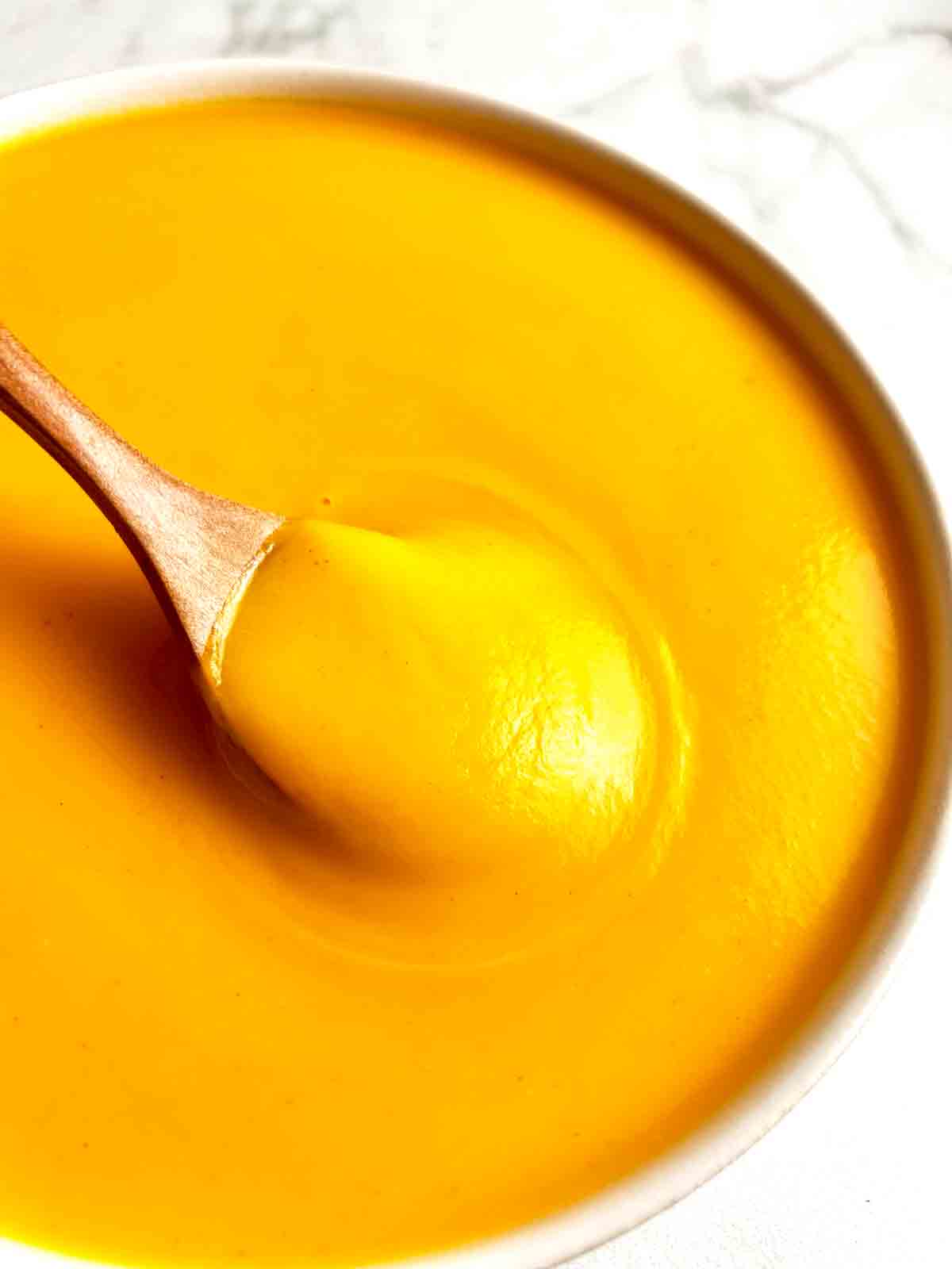 close up of spoon lifting soup from bowl showing the smooth texture of the soup.