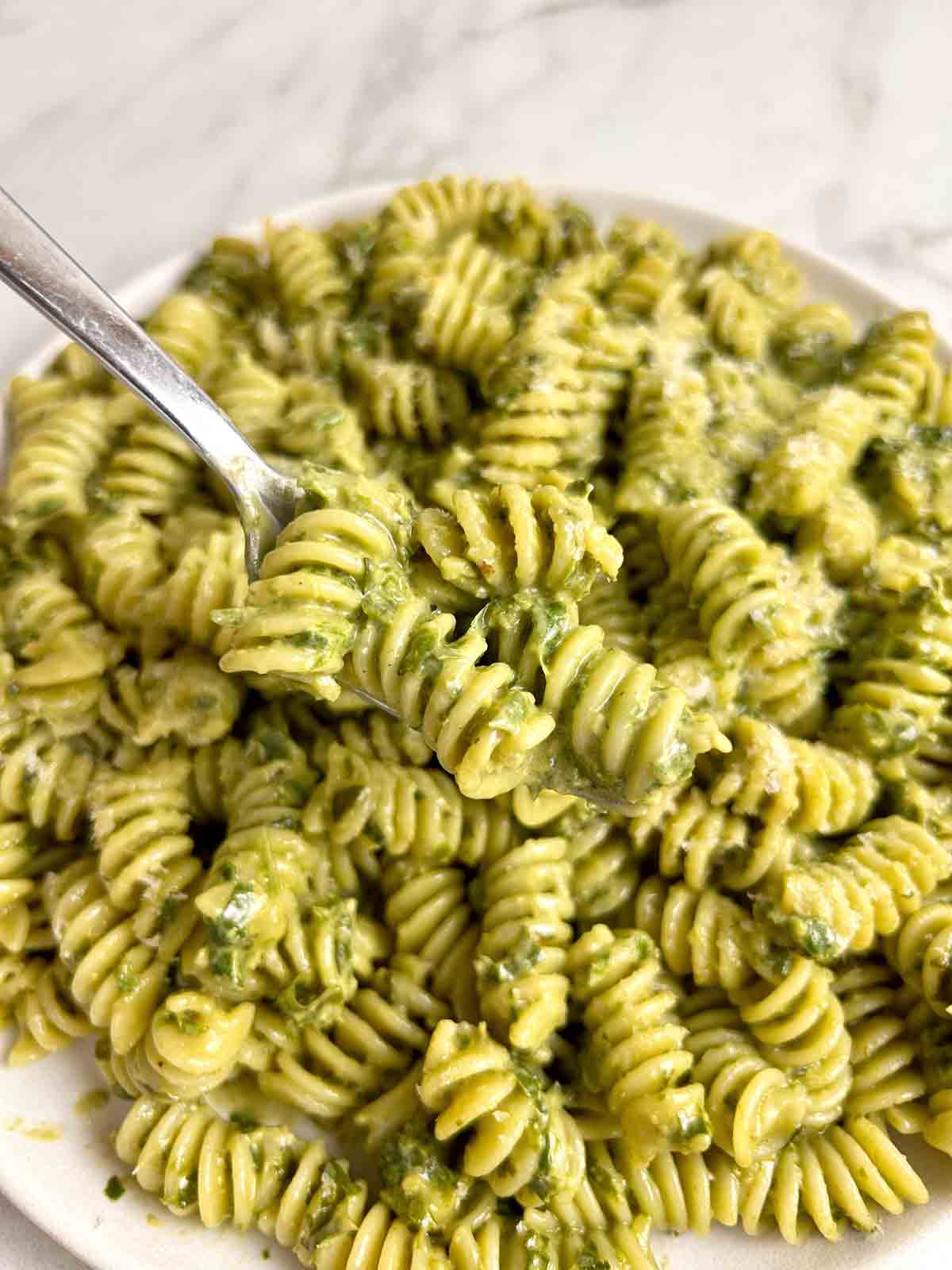 fork lifting pesto pasta from plate.