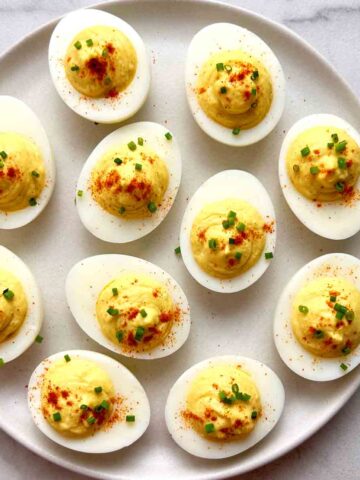 plate of deviled eggs with paprika and chopped chives.