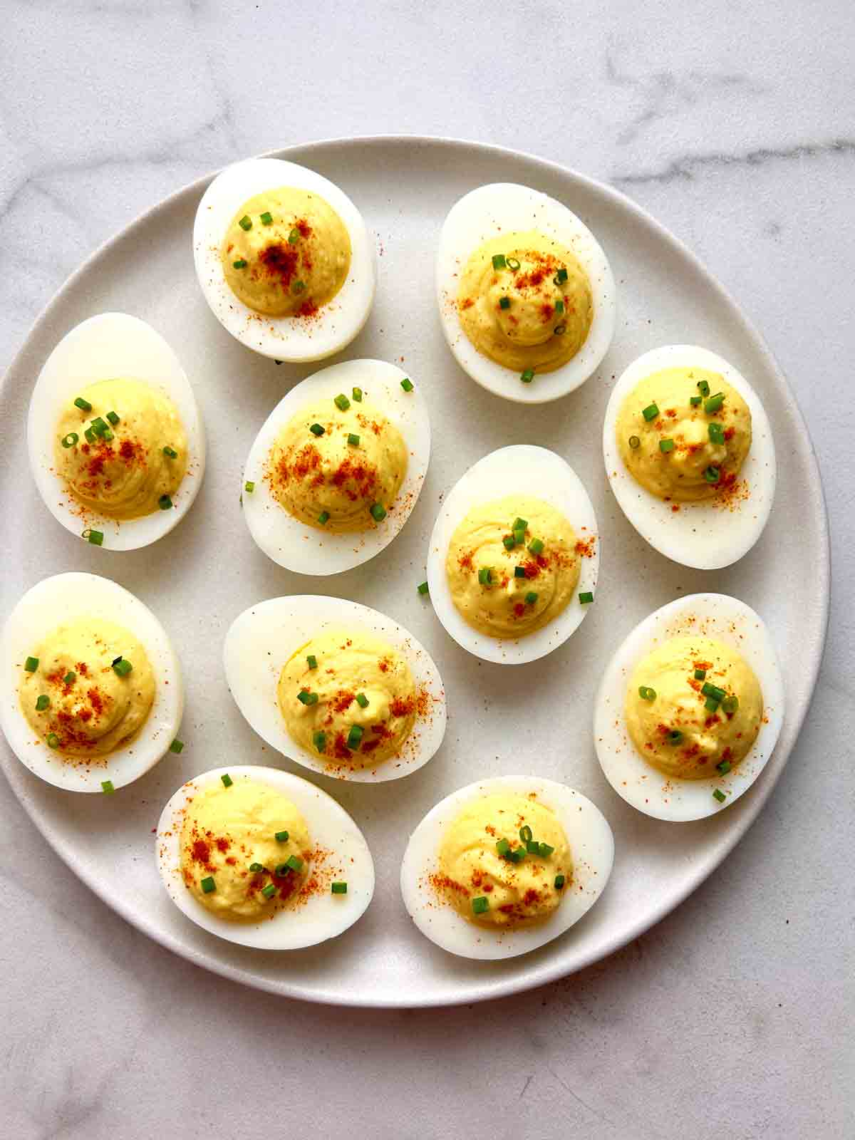 plate of deviled eggs with paprika and chopped chives.