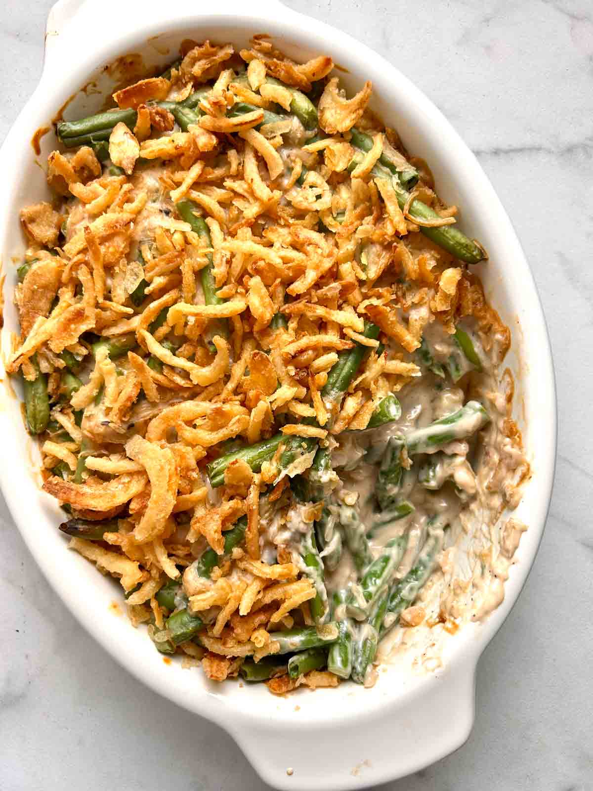 close up of green bean casserole with portion of it scooped out of baking dish.