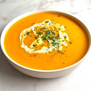 bowl of pumpkin soup garnished with parsley, pepper, and cream.