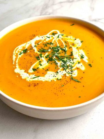 bowl of pumpkin soup garnished with parsley, pepper, and cream.