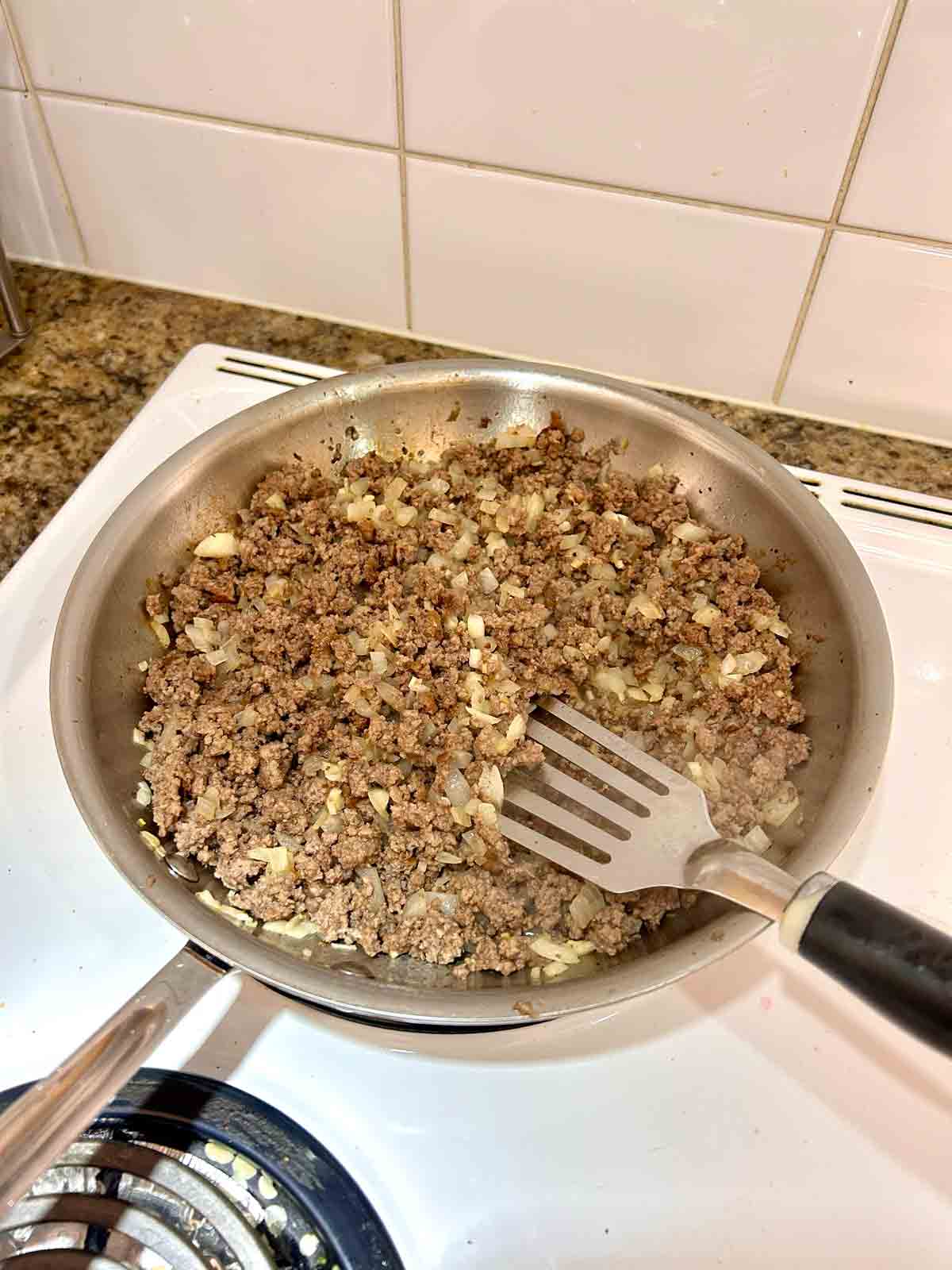 ground beef, onions, and garlic being sautéed in skillet.