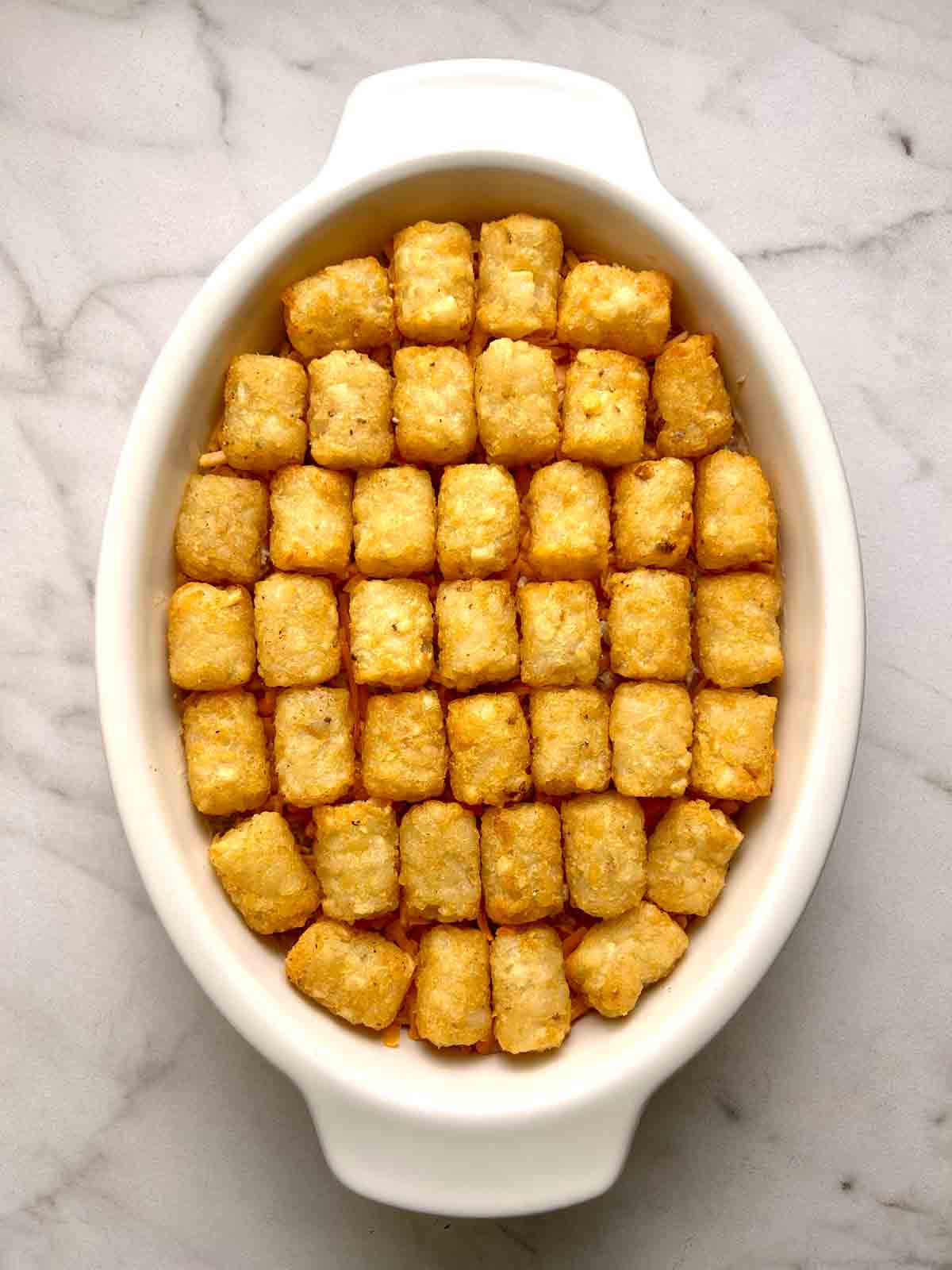 tater tots and cheese spread on top of casserole.