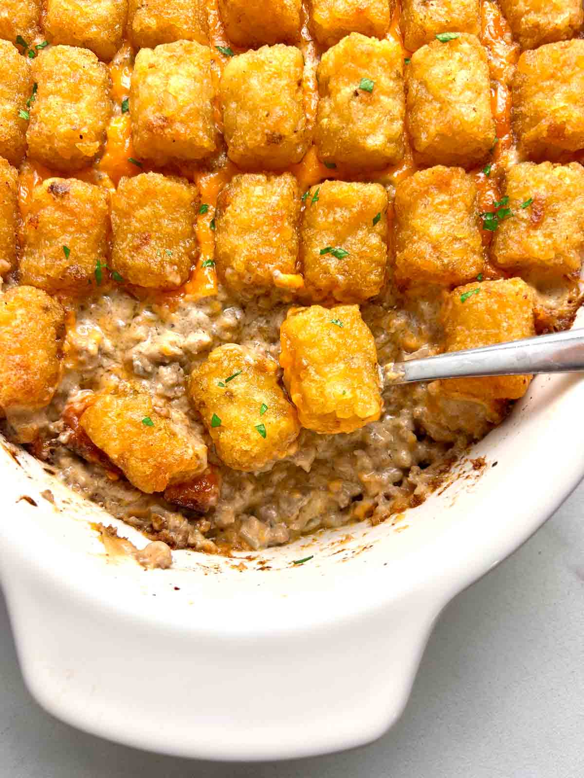 close up of tater tot casserole with spoon scooping some of it out.