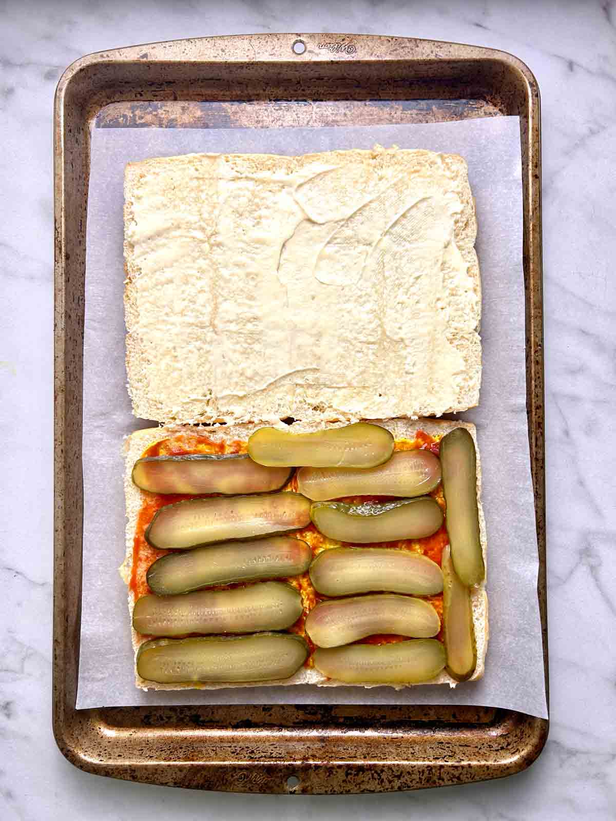 condiments spread on buns nad pickles added.