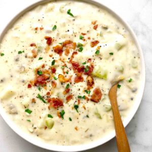 bowl of clam chowder with crispy bacon and parsley sprinkled on top.