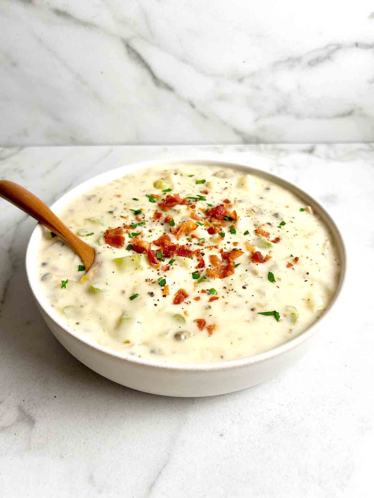 bowl of clam chowder with crispy bacon and parsley sprinkled on top.