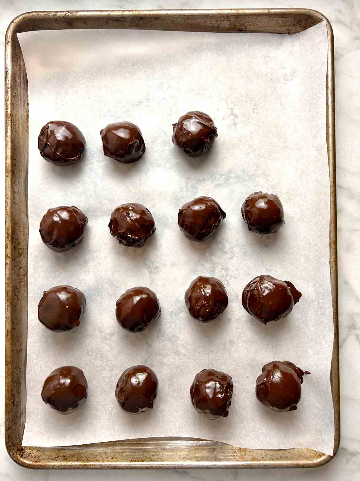 balls covered in chocolate and arranged on baking sheet.